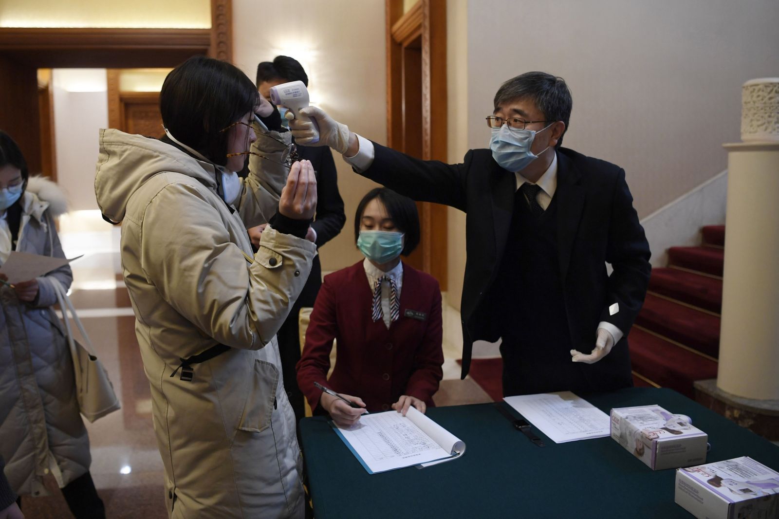 Na snímke muž meria teplotu novinárke pred stretnutím generálneho riaditeľa Svetovej zdravotníckej organizácie (WHO) Tedrosa Adhana Ghebreyesusa a čínskeho ministra zahraničných vecí Wang I v Pekingu 28. januára 2020.